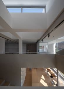 A modern workspace with glass walls and concrete elements, featuring a high ceiling and skylight.