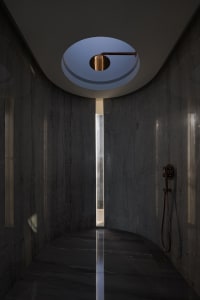 Modern bathroom with dark marble walls and floor, featuring a circular skylight and a black shower head.