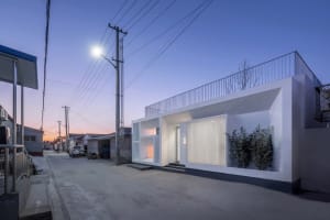 Modern minimalist house with concrete frame and metal railings, illuminated by a streetlight at dusk.