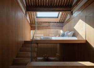 A modern bedroom featuring wooden elements, with a lofted bed and glass railing.