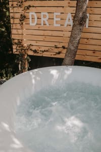 A close-up view of a bubbling outdoor hot tub surrounded by lush greenery with a wooden fence and the word 'DREAM' in the bac