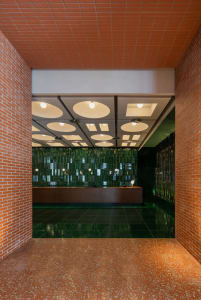 Modern reception area with brick and concrete walls, a green-glass feature wall, and a reception counter.