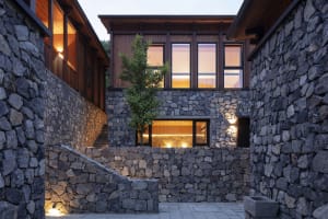 Modern building with stone and wood exterior, illuminated windows, and steps.