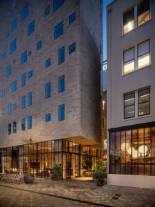 Nighttime view of a modern apartment building with concrete and glass facade, featuring numerous windows and a bicycle parkin