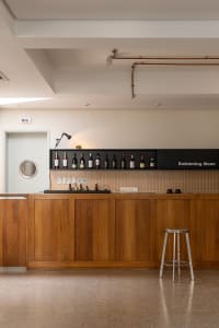 A modern bar area with wooden cabinets, bottles on shelves, and a single stool.