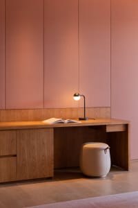 A modern desk space with a wood finish, featuring an open book and a table lamp.