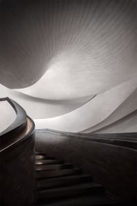 A sleek, modern staircase with curved metal steps and a dark wood railing, set against a textured, light-colored wall.