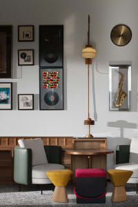 Modern living room featuring wooden furniture, colorful stools, and a wall gallery with musical memorabilia.