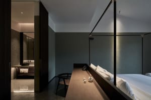 A modern bedroom with dark interior design features a wooden desk, a metal canopy bed, and a minimalist design aesthetic.