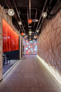 A modern industrial corridor with concrete walls, metal light fixtures, and red geometric patterns on the wall.