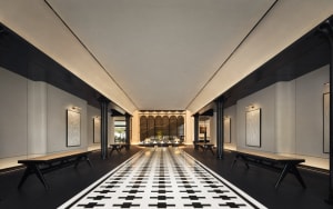 A modern hotel lobby with concrete walls, black sand floor tiles, and a long black and white checkered floor leading to a sea