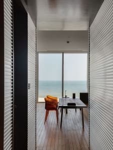 Modern office with wooden flooring, large windows overlooking the sea, and minimalist design.