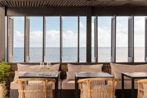 A coastal restaurant bar with a view of the ocean, featuring wooden furniture, stone accents, and curtains. Two wine glasses 