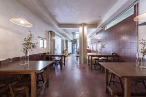 Minimalist cafe interior with exposed concrete walls, wood tables, and terrazzo floor tiles.