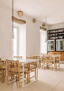 A minimalist restaurant dining room with white walls, wooden tables and chairs, and hanging stone decor.