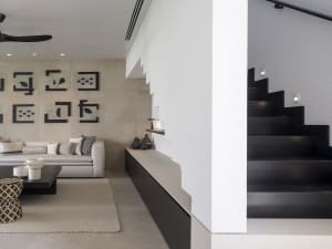 A modern living room featuring concrete walls and flooring, with a white sofa and abstract wall art.