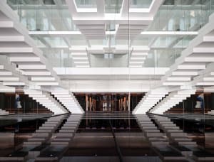 A modern office lobby with glass staircases and a reflective floor.