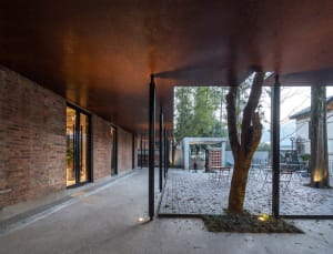 An industrial-style architectural interior with brick walls and a tree in the courtyard.