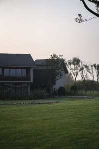 A modern house with concrete and glass exterior surrounded by greenery.