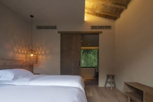 Bedroom with minimalist decor, featuring a wooden bed and a wicker pendant lamp.