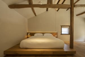 A minimalist bedroom featuring a wooden platform bed with white bedding and a window