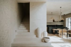 A minimalist kitchen with concrete elements, featuring a dining table and pendant lights.