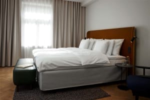 A modern minimalist bedroom with white linen bedding, a comfortable bed with multiple pillows, and a warm, inviting ambiance.