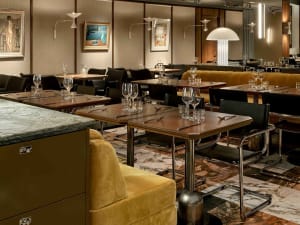 A modern restaurant interior featuring a wooden counter with chairs and tables.