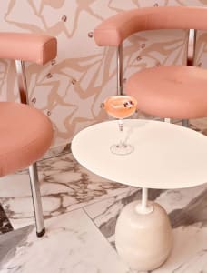 A modern bar setting featuring a pink upholstered chair, a round marble tabletop, and a cocktail glass.