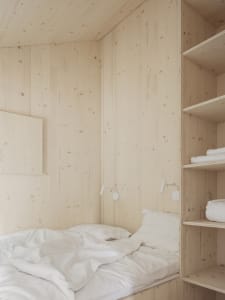 A minimalist bedroom with white wood walls and a bed with white bedding.