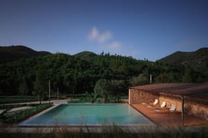 A serene pool area in a natural landscape setting with hills, trees, and a clear blue sky above.