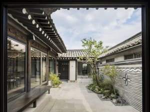 Traditional Korean yard with wooden structures, glass walls, and stone paths.