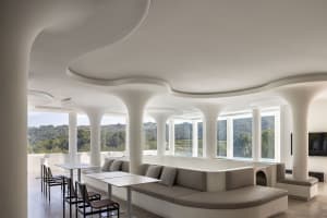 A minimalist restaurant with glass walls, concrete seating, and a set of tables.