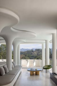 A modern living room with a concrete ceiling and floor, featuring a curved sofa, a round black coffee table, and a view of th