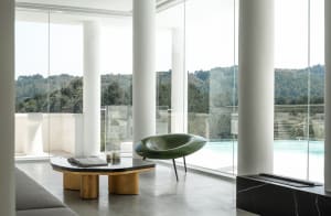 Modern minimalist living room featuring glass walls, concrete floor, and green seating area.