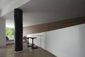 Minimalist interior with concrete barstools and a large black column.