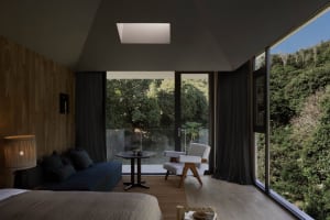 Modern minimalist bedroom with wood elements and a view of the forest through large windows.