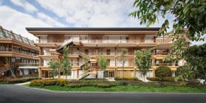 A multi-story residential building with wooden frames and glass panels surrounded by greenery.