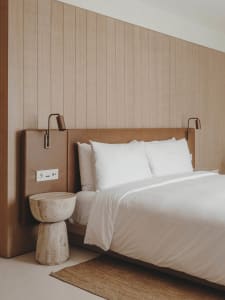 Minimalist bedroom with wooden walls, white bedding, and textured side table.