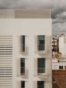 Modern residential building with white concrete exterior and white metal railings on balconies against a cloudy sky.