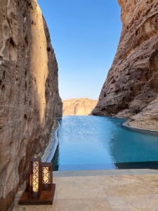 A serene view of a natural stone-faced poolside area with a large blue lake surrounded by towering rock formations under a cl