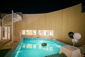 A minimalist room featuring a swimming pool surrounded by a tiled floor and walls. The room has a spiral staircase and a tabl