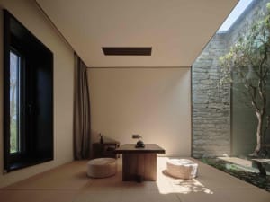 A minimalist living room with wooden furniture and a stone wall.