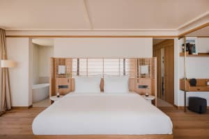 Minimalist hotel bedroom featuring a wooden bed with white bedding and a wooden headboard.