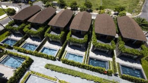 Aerial view of modern residential homes with private pools surrounded by greenery and terraced roofs.