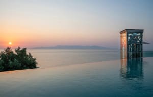 Modern infinity pool with metal and glass construction overlooking the ocean at sunset.