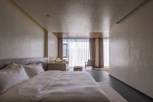 A minimalist bedroom with textured walls, a large window, and white bedding.