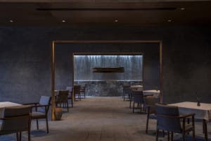 A minimalist restaurant interior featuring a waterfall wall made of metal and stone.