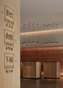 Modern lobby featuring wooden walls and flooring, with ceiling lights and signage.