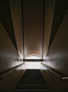 View looking up inside a modern, industrial tunnel with concrete walls and a natural light source at the end.
